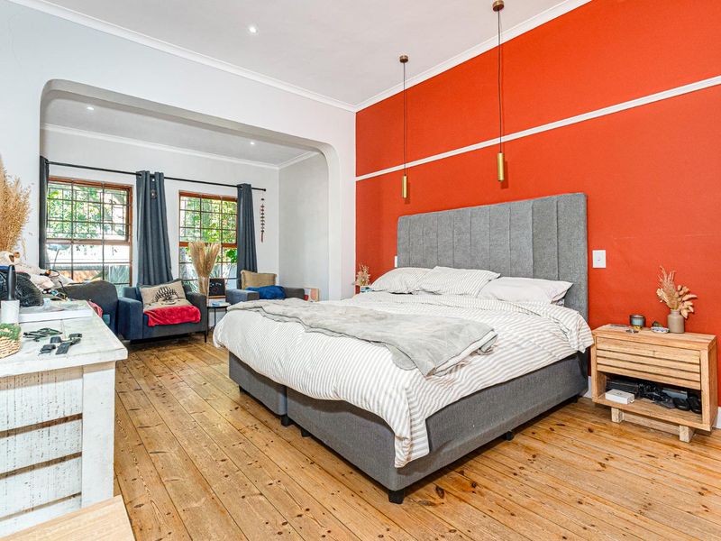 Spacious bedroom featuring original hardwood flooring, a bold accent wall, and large timber-framed windows that provide ample natural light.