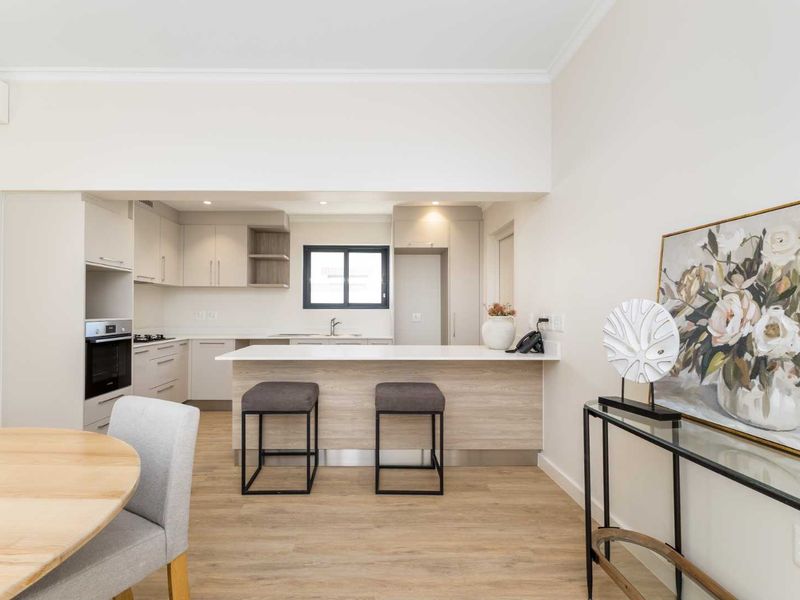 Modern open-plan kitchen featuring sleek cabinetry, stone countertops, a breakfast bar, and integrated appliances, seamlessly flowing into the dining area.