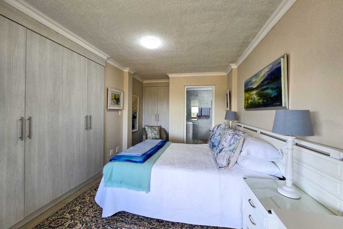 A well-maintained bedroom featuring extensive built-in cabinetry, crown molding, and an en-suite bathroom visible through the doorway.