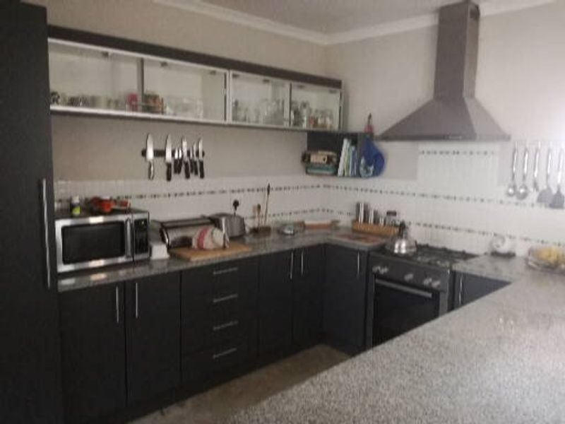 A functional kitchen featuring dark cabinetry, granite countertops, a tiled backsplash, and integrated stainless steel appliances including an oven, hob, and extractor fan.