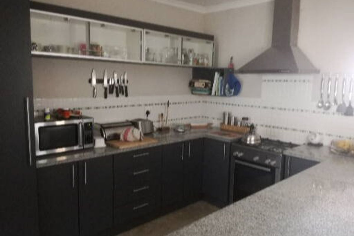 A functional kitchen featuring dark cabinetry, granite countertops, a tiled backsplash, and integrated stainless steel appliances including an oven, hob, and extractor fan.
