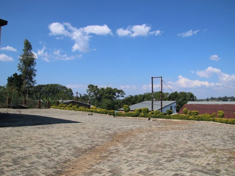 Spacious paved outdoor area featuring established hedging, perimeter electric fencing, and views of surrounding industrial structures under a clear sky.