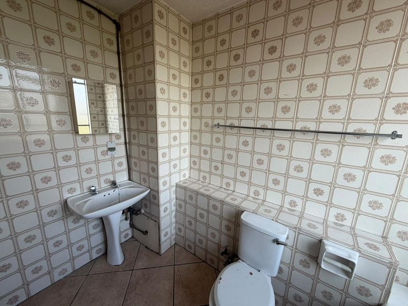 A dated bathroom featuring a pedestal washbasin, toilet, and full-height patterned wall tiling, offering significant potential for modernization and renovation.