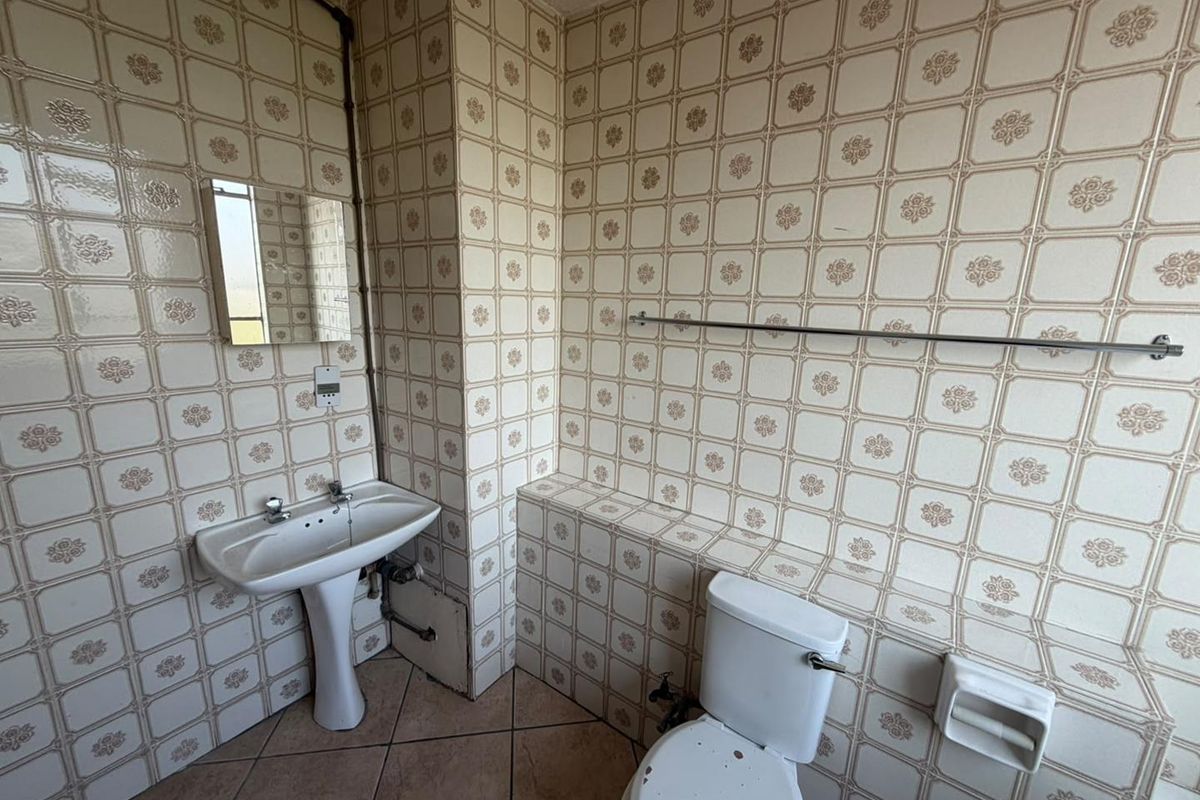 A dated bathroom featuring a pedestal washbasin, toilet, and full-height patterned wall tiling, offering significant potential for modernization and renovation.