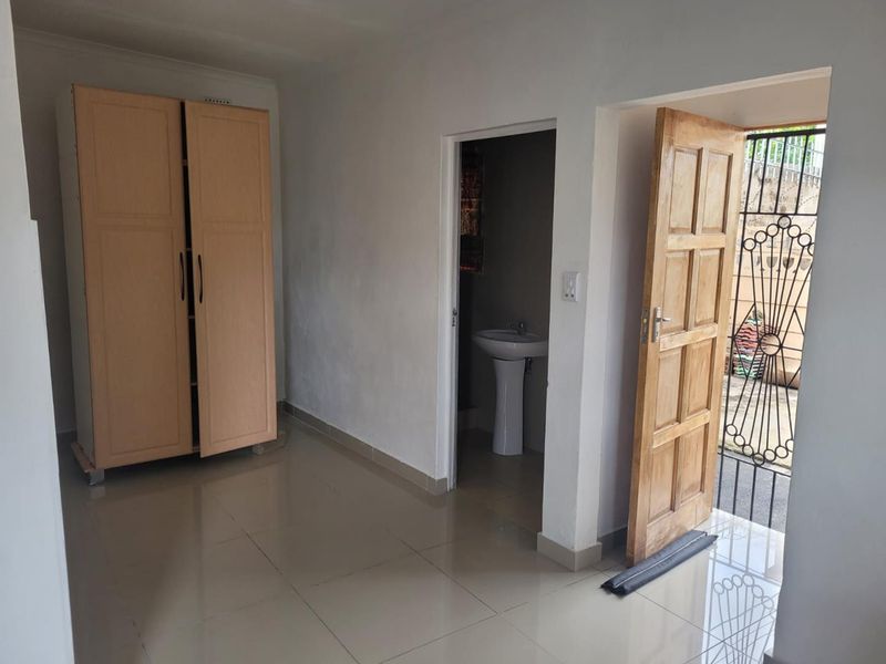 A bedroom featuring tiled flooring and an en-suite bathroom with a pedestal basin, leading directly to an exterior security gate.