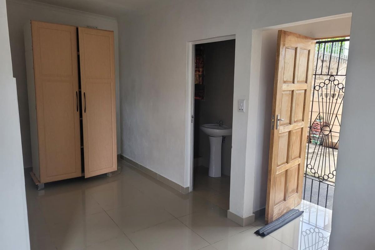A bedroom featuring tiled flooring and an en-suite bathroom with a pedestal basin, leading directly to an exterior security gate.