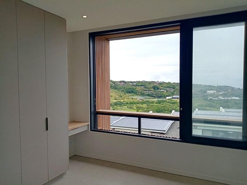 A modern, bright bedroom featuring built-in cupboards, a sleek integrated desk, and large windows offering expansive landscape views.