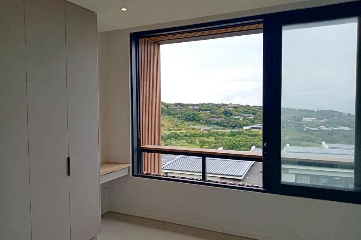 A modern, bright bedroom featuring built-in cupboards, a sleek integrated desk, and large windows offering expansive landscape views.