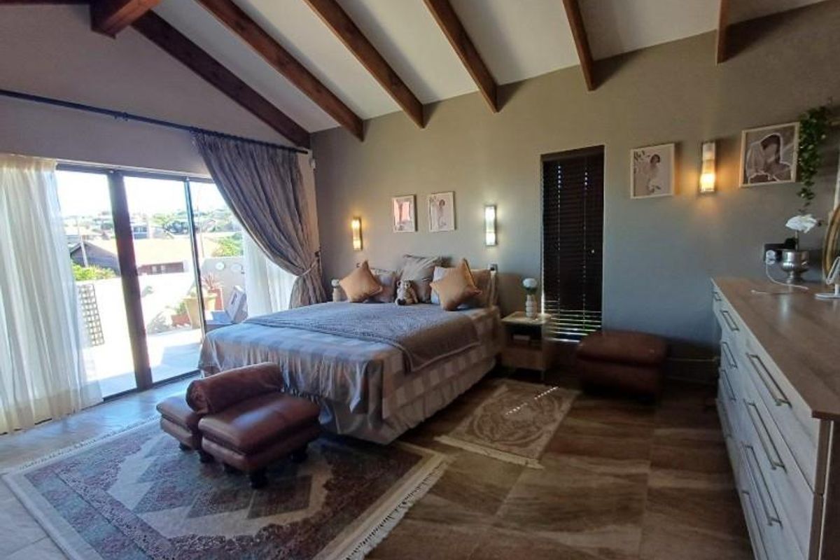 Spacious bedroom featuring vaulted ceilings with exposed timber beams, tiled flooring, and large sliding glass doors providing access to an outdoor balcony area.