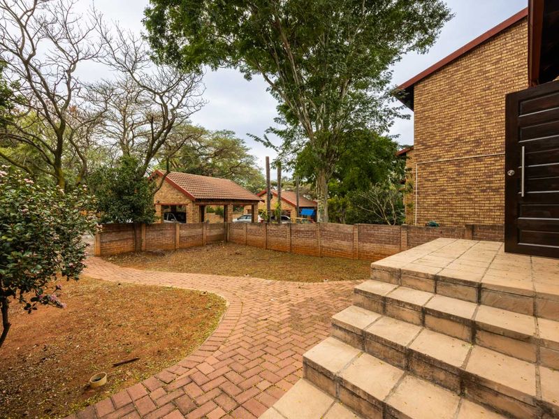 A rear exterior view of the townhouse featuring a paved walkway, tiled entrance steps, and a private garden area enclosed by a brick boundary wall.