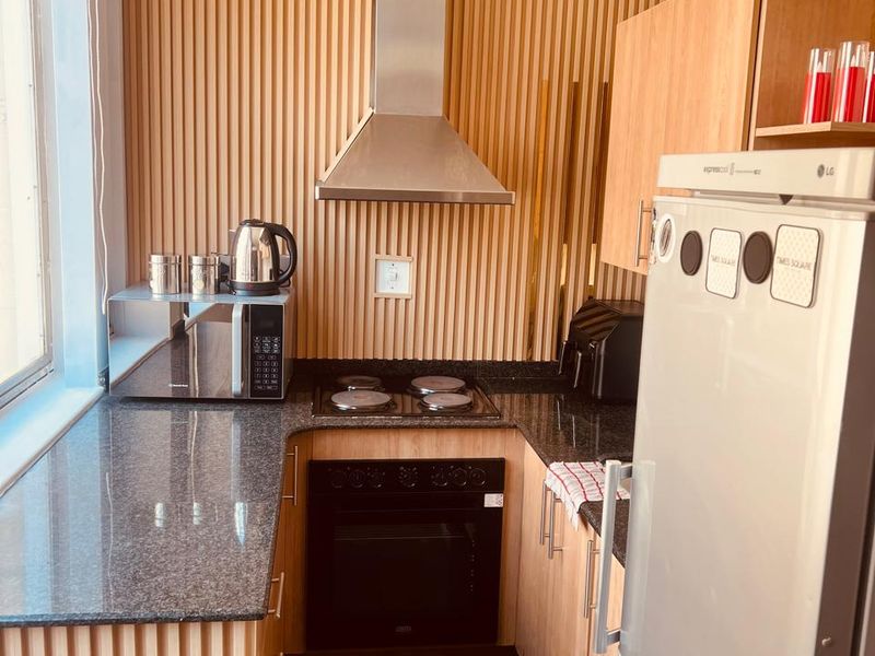A compact, modern kitchen featuring granite countertops, built-in oven, electric hob, stainless steel extractor fan, and stylish timber slat wall paneling.