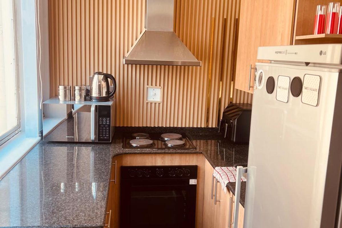 A compact, modern kitchen featuring granite countertops, built-in oven, electric hob, stainless steel extractor fan, and stylish timber slat wall paneling.