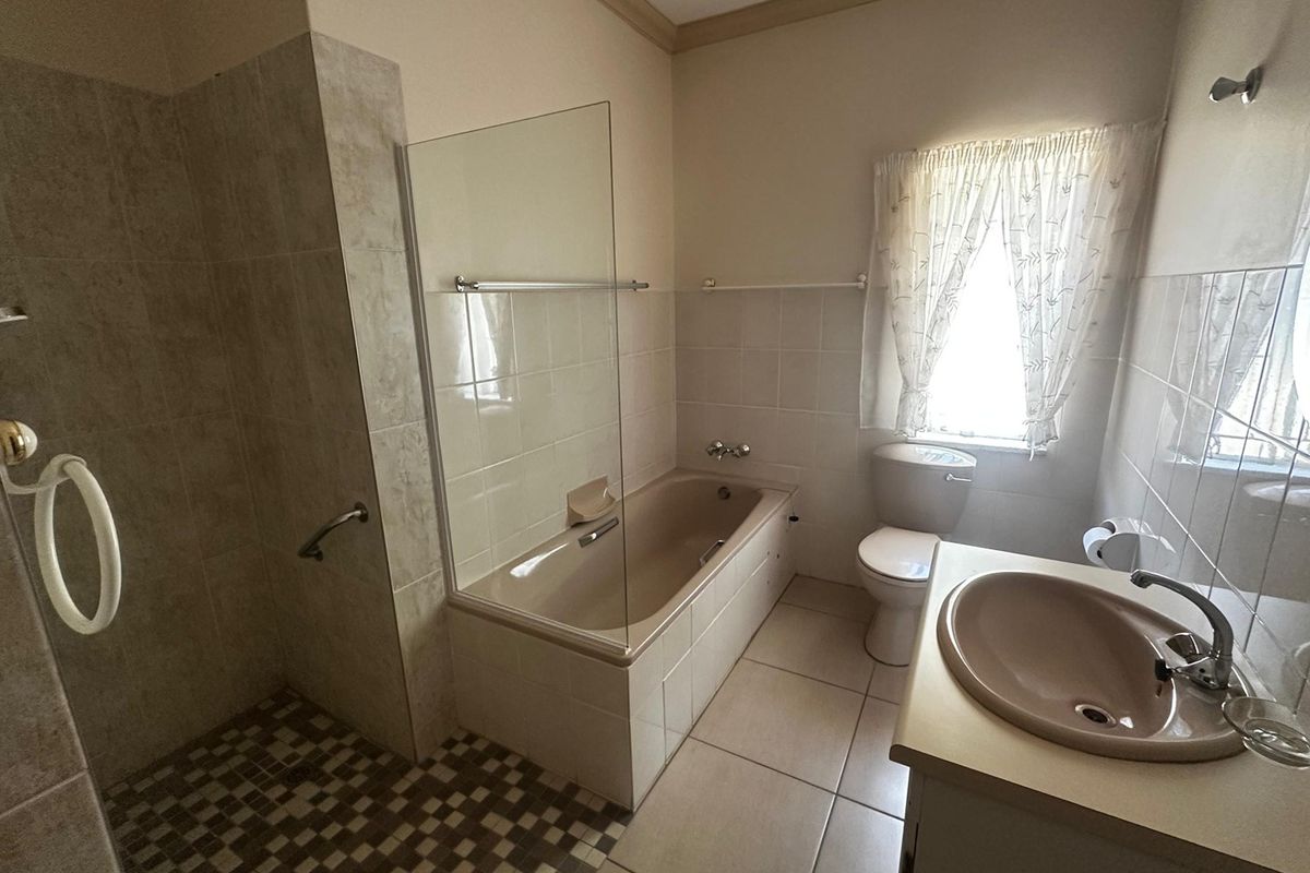 A functional bathroom featuring a built-in bathtub, separate tiled shower enclosure, pedestal washbasin, and toilet with neutral wall and floor tiling.