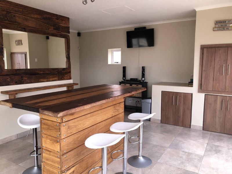 A dedicated home bar area featuring a custom wooden bar counter, built-in storage cabinetry, and neutral tiled flooring.