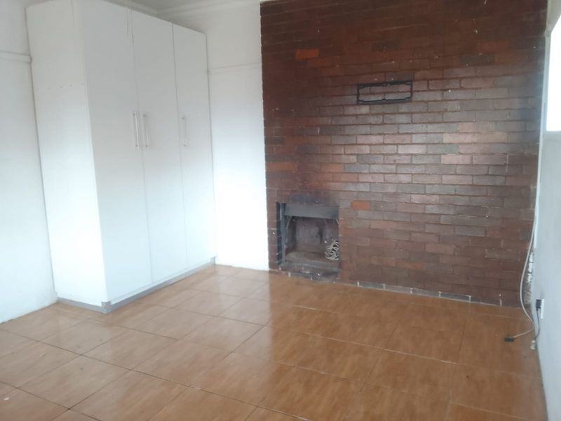An empty bedroom featuring tiled flooring, built-in cupboards, and a prominent brick fireplace, offering a blank canvas for personalization.