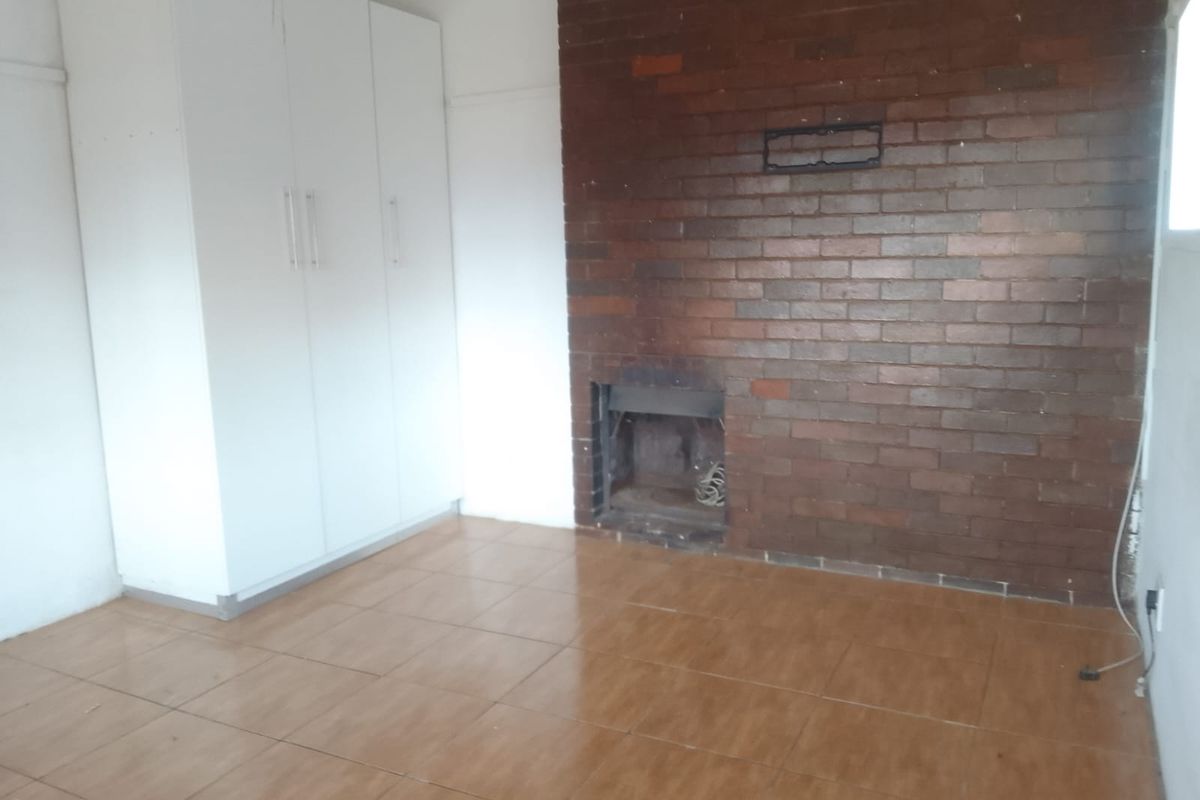 An empty bedroom featuring tiled flooring, built-in cupboards, and a prominent brick fireplace, offering a blank canvas for personalization.