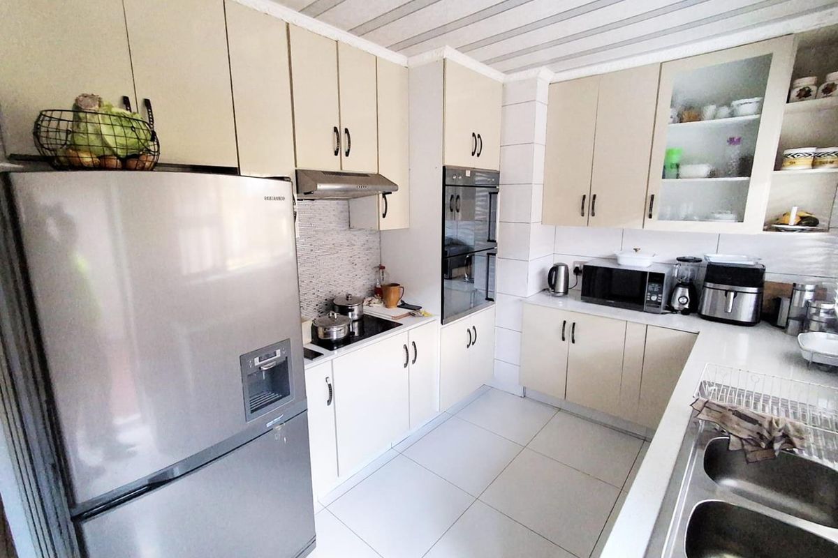 A functional kitchen featuring cream-toned cabinetry, built-in oven, electric hob, extractor fan, and a double bowl sink with tiled flooring and backsplash.