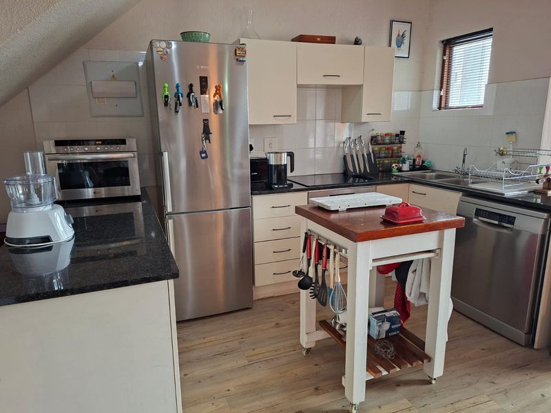 Functional kitchen featuring granite countertops, built-in oven, hob, and ample cabinetry, set against a tiled backsplash with laminate flooring.