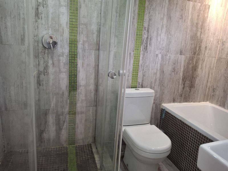 A functional bathroom featuring a glass shower enclosure, built-in bathtub, and modern ceramic toilet with decorative mosaic tile accents.