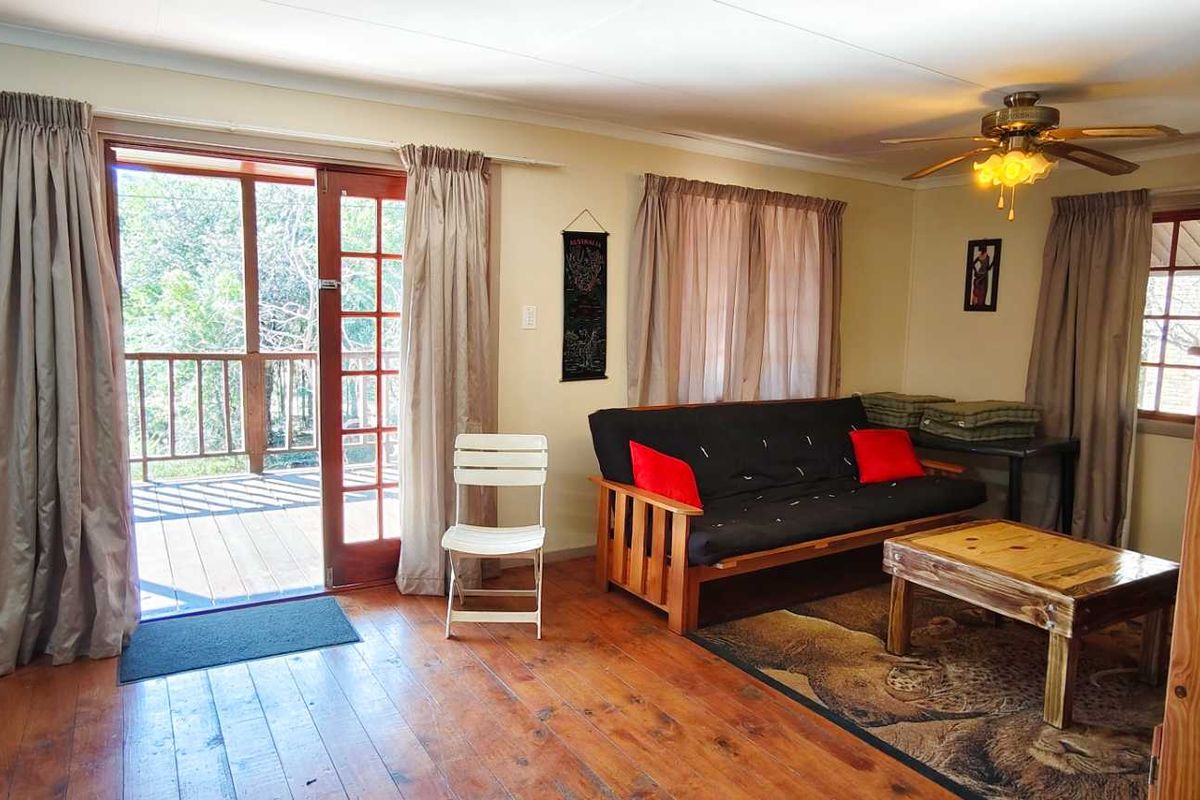 A living room featuring timber flooring, a ceiling fan, and direct access to an outdoor deck through wooden framed glass doors.