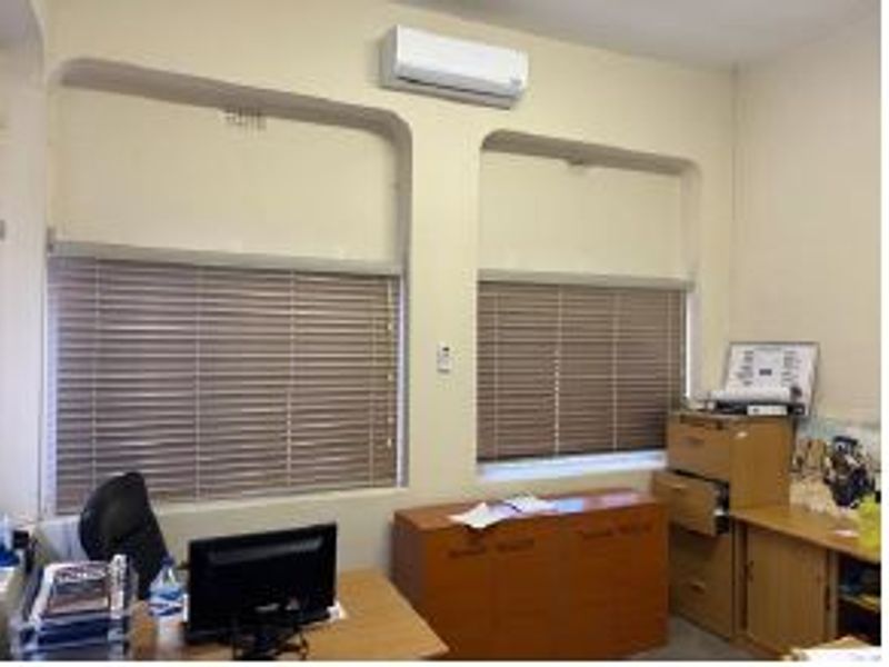 A functional office space featuring dual recessed windows with venetian blinds and a wall-mounted split-system air conditioning unit.