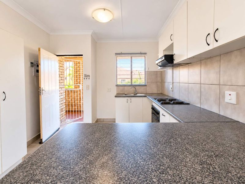 A functional kitchen featuring built-in cabinetry, laminate countertops, an electric hob, and an integrated oven, with direct access to an outdoor area.