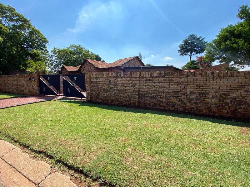 Front view of the property featuring a well-maintained lawn, brick boundary wall, and secure metal driveway gate leading to the house.