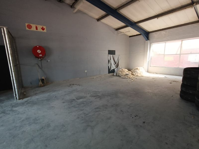 An open-plan industrial utility space featuring concrete flooring, exposed steel structural beams, and a wall-mounted fire hose reel.