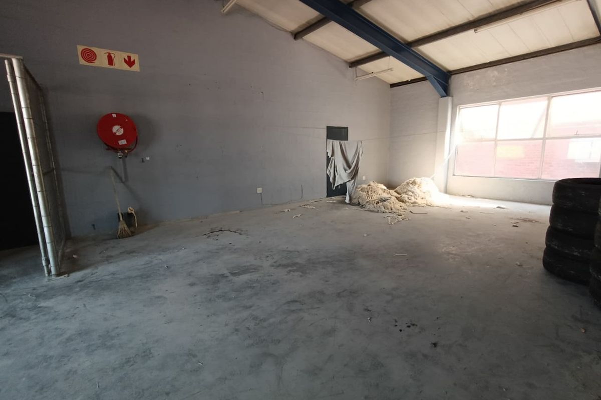An open-plan industrial utility space featuring concrete flooring, exposed steel structural beams, and a wall-mounted fire hose reel.