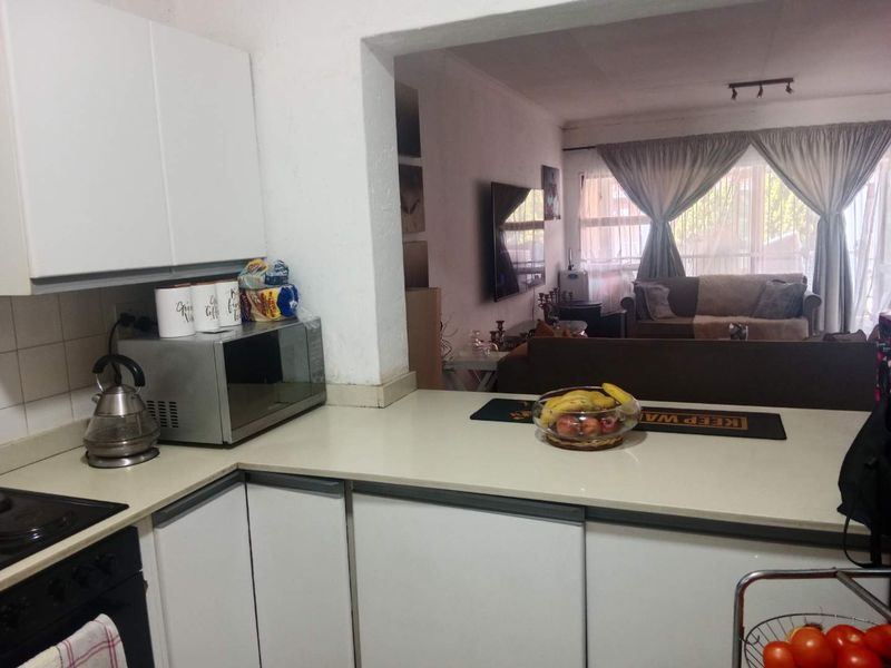 Open-plan kitchen and living area featuring white cabinetry, stone countertops, and a convenient pass-through window connecting the kitchen to the lounge.