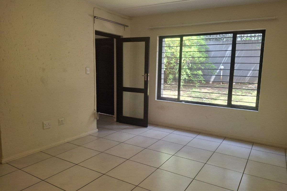 An empty living room featuring tiled flooring, security bars on the window, and direct access to an outdoor area.