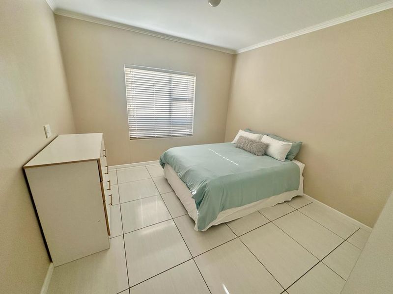 A clean and well-maintained bedroom featuring neutral wall tones, large format floor tiles, and fitted venetian blinds.