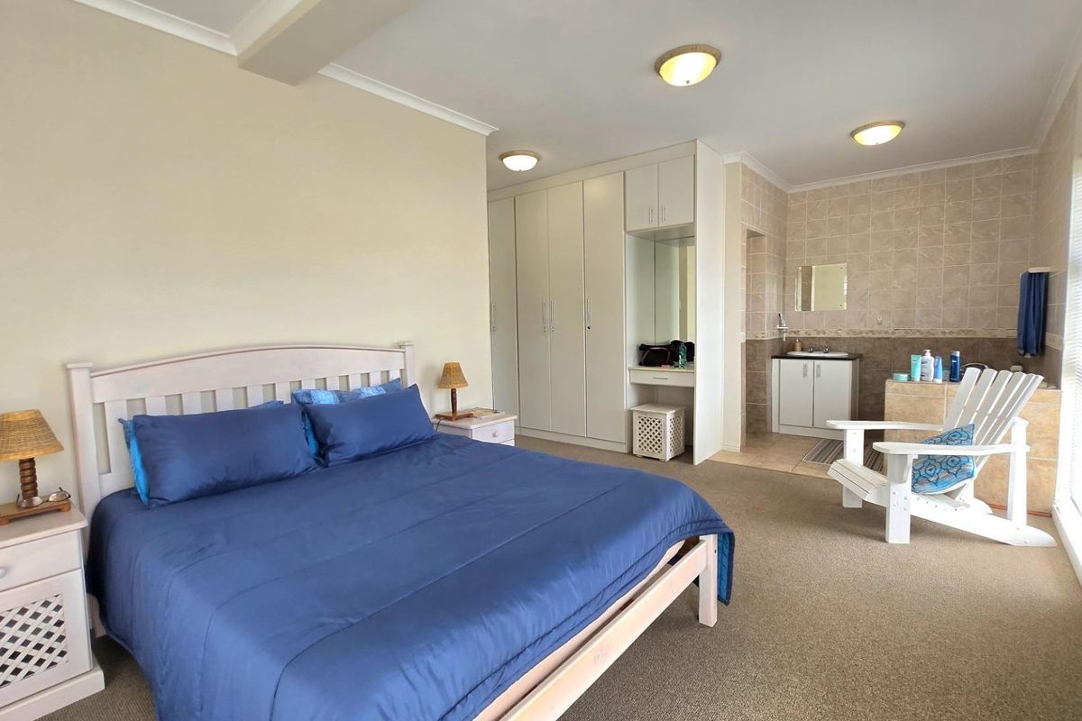 Spacious bedroom featuring built-in cupboards, a dedicated vanity area, and an open-plan en-suite bathroom with tiled finishes.