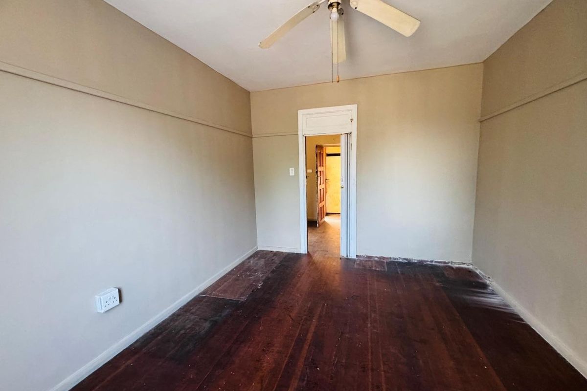 An empty bedroom featuring original timber flooring, a ceiling fan, and picture rails, offering a blank canvas for renovation or interior design updates.