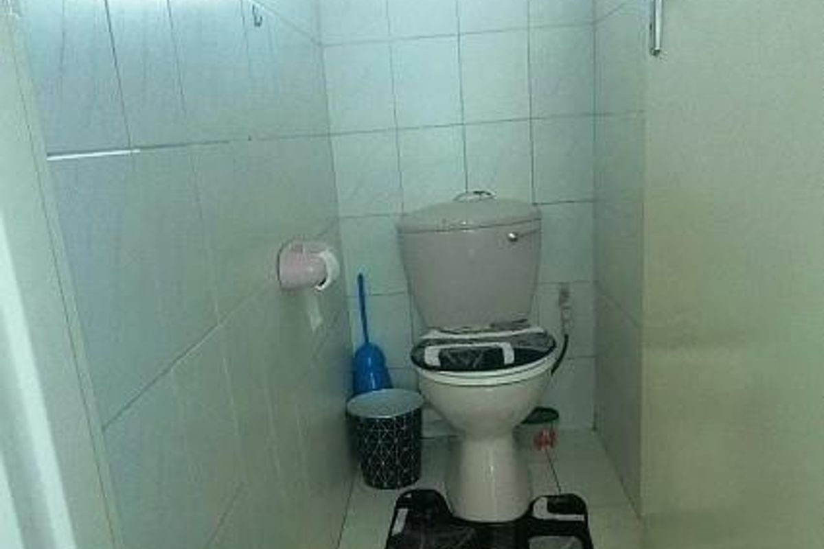 A compact bathroom featuring a standard toilet, tiled walls, and tiled flooring with a small window for natural light.