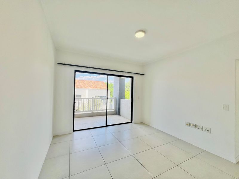 A bright, empty bedroom featuring neutral tiled flooring, a ceiling light, and a sliding glass door providing direct access to a private balcony.
