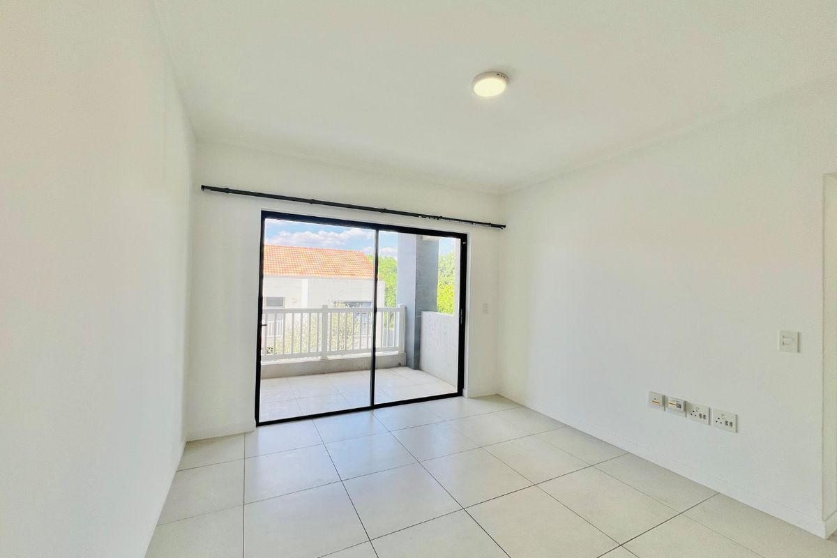 A bright, empty bedroom featuring neutral tiled flooring, a ceiling light, and a sliding glass door providing direct access to a private balcony.