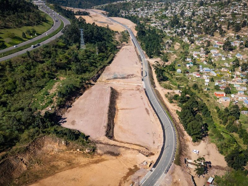 An aerial view of a large, cleared industrial development site adjacent to a major highway and residential area.