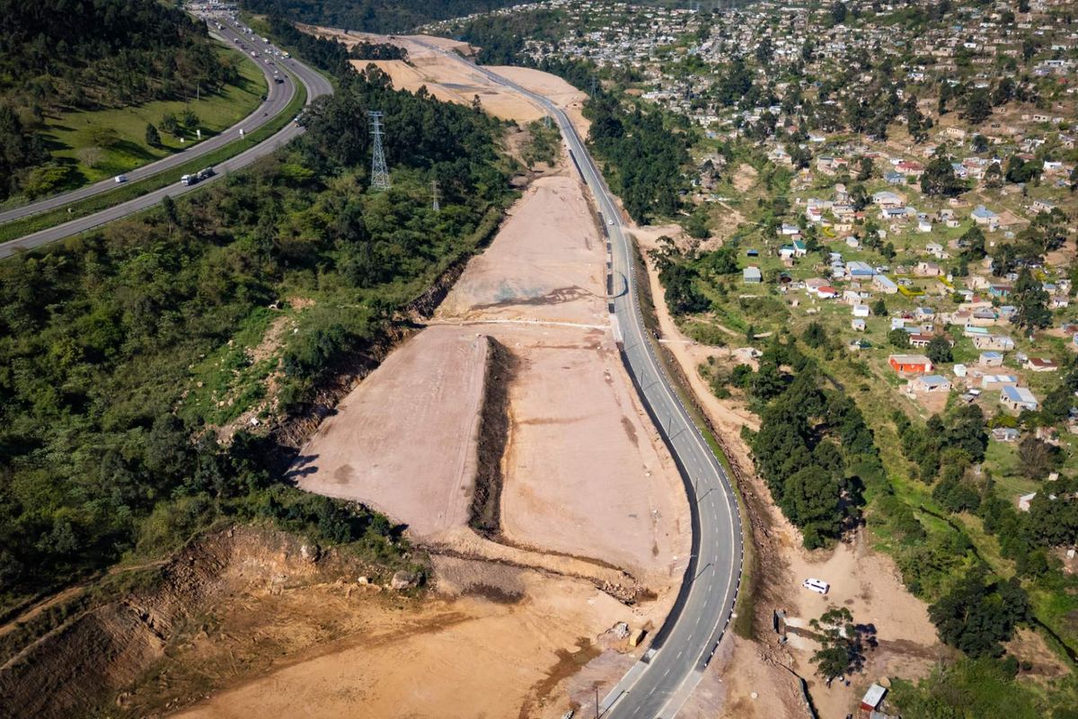 An aerial view of a large, cleared industrial development site adjacent to a major highway and residential area.