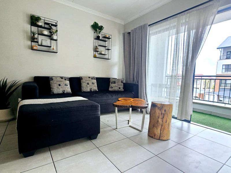 A bright living room featuring tiled flooring and a large sliding glass door that provides direct access to an outdoor balcony area.