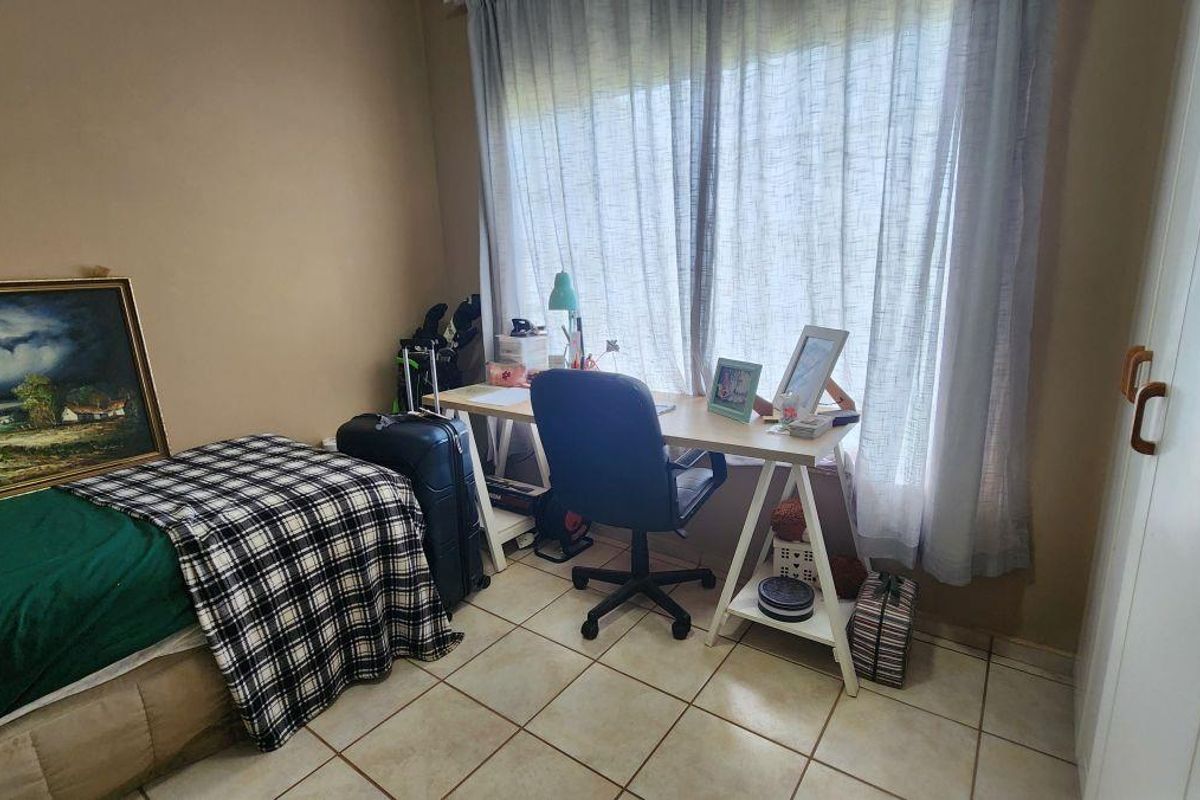 A functional bedroom featuring tiled flooring, built-in cupboards, and a large window with curtaining, providing natural light to the space.