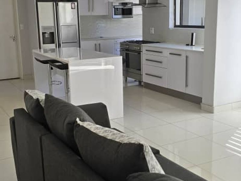 Modern open-plan living area featuring a sleek kitchen with a central island, stainless steel appliances, and polished tiled flooring throughout.