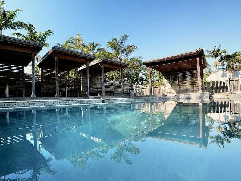 A well-maintained outdoor pool area featuring multiple wooden cabanas and timber privacy screening, creating a relaxed resort-style atmosphere.