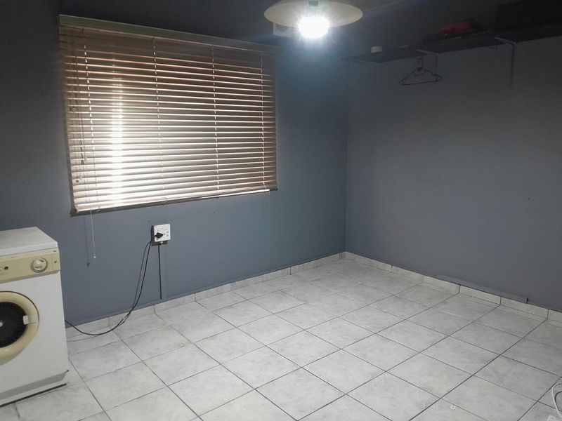 A vacant bedroom featuring tiled flooring, grey painted walls, and venetian blinds, offering a blank canvas for potential interior design updates.
