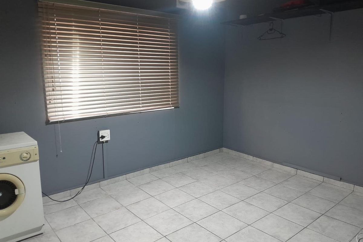 A vacant bedroom featuring tiled flooring, grey painted walls, and venetian blinds, offering a blank canvas for potential interior design updates.