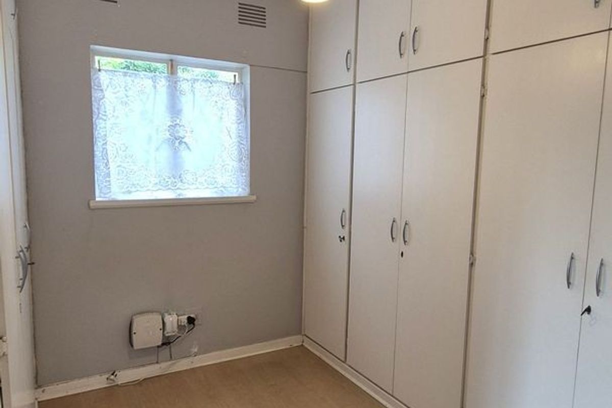 A compact bedroom featuring extensive built-in floor-to-ceiling cabinetry, light wood-look flooring, and a single pendant light fixture.