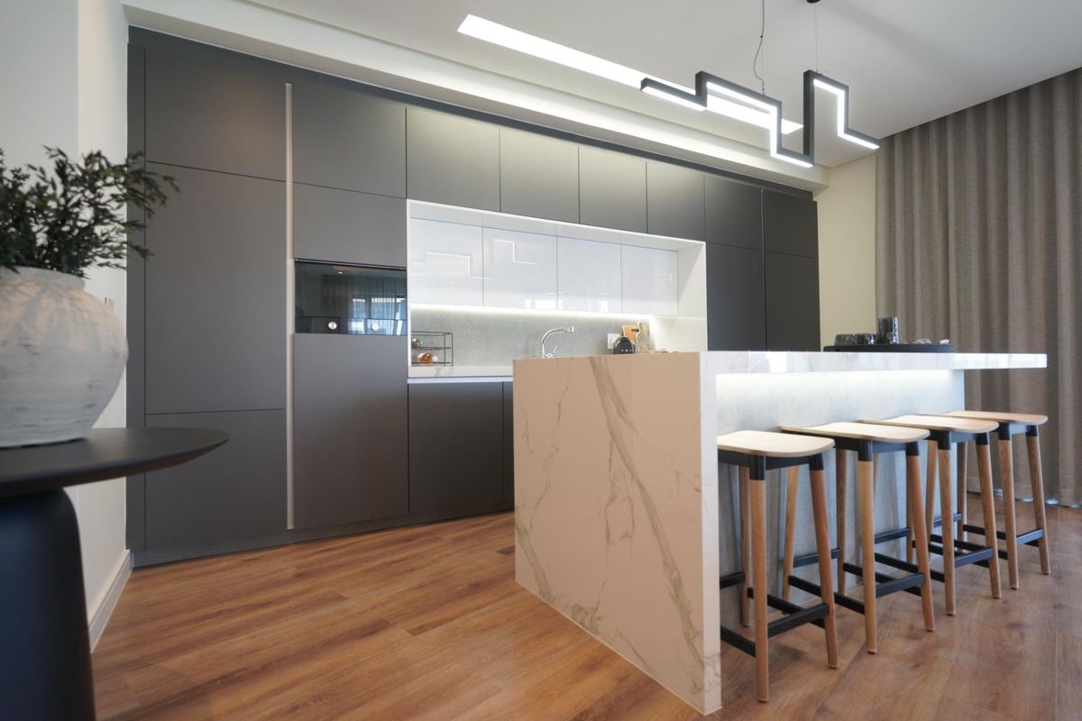 Modern kitchen featuring sleek dark cabinetry, a marble-look island with integrated lighting, and high-end built-in appliances.