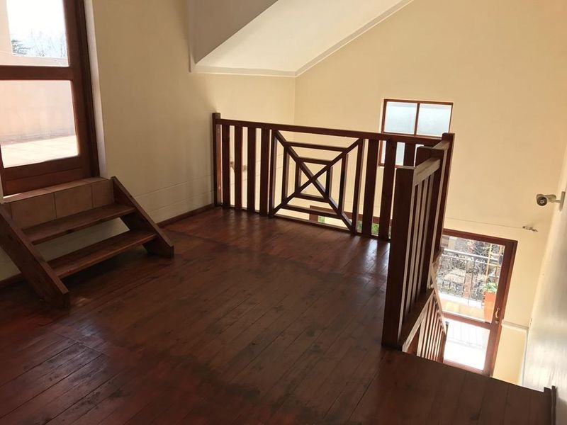 An empty mezzanine living area featuring timber flooring, a wooden balustrade, and a staircase leading to an outdoor balcony.