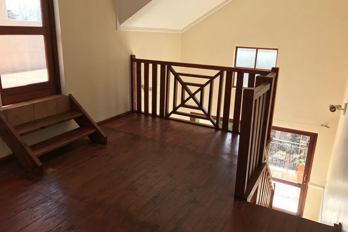 An empty mezzanine living area featuring timber flooring, a wooden balustrade, and a staircase leading to an outdoor balcony.