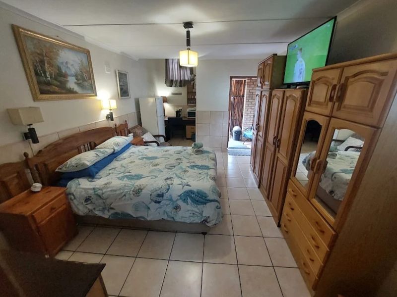 A bedroom featuring tiled flooring and wall-mounted lighting, with an adjoining area visible in the background.